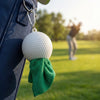 Golf ball keychain with green towel attached to a bag on a golf course